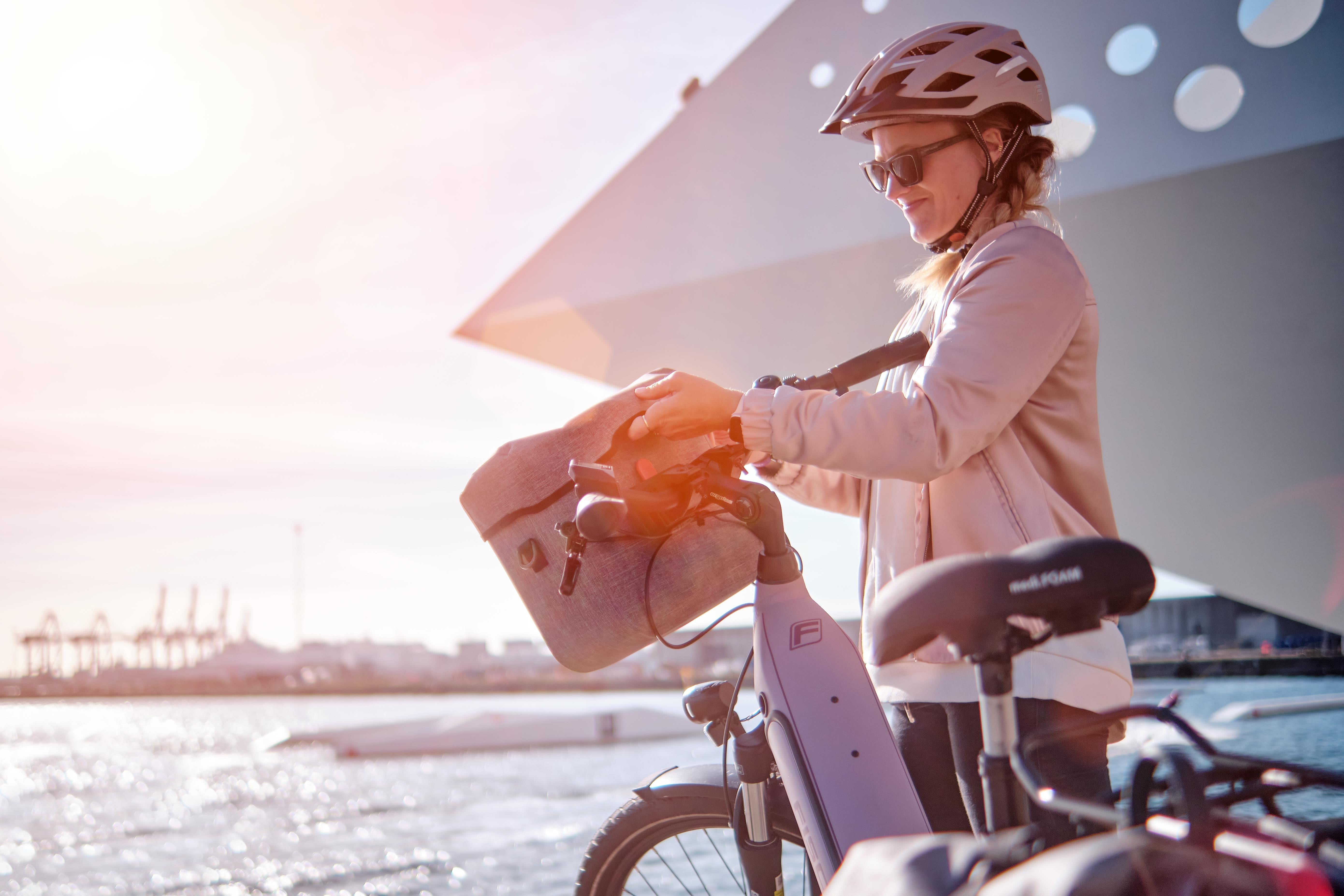 E-Bike Ausflug: Eine Radfahrerin befestigt ihre Tasche an einem Fischer City E-Bike Cita bei strahlendem Sonnenschein.